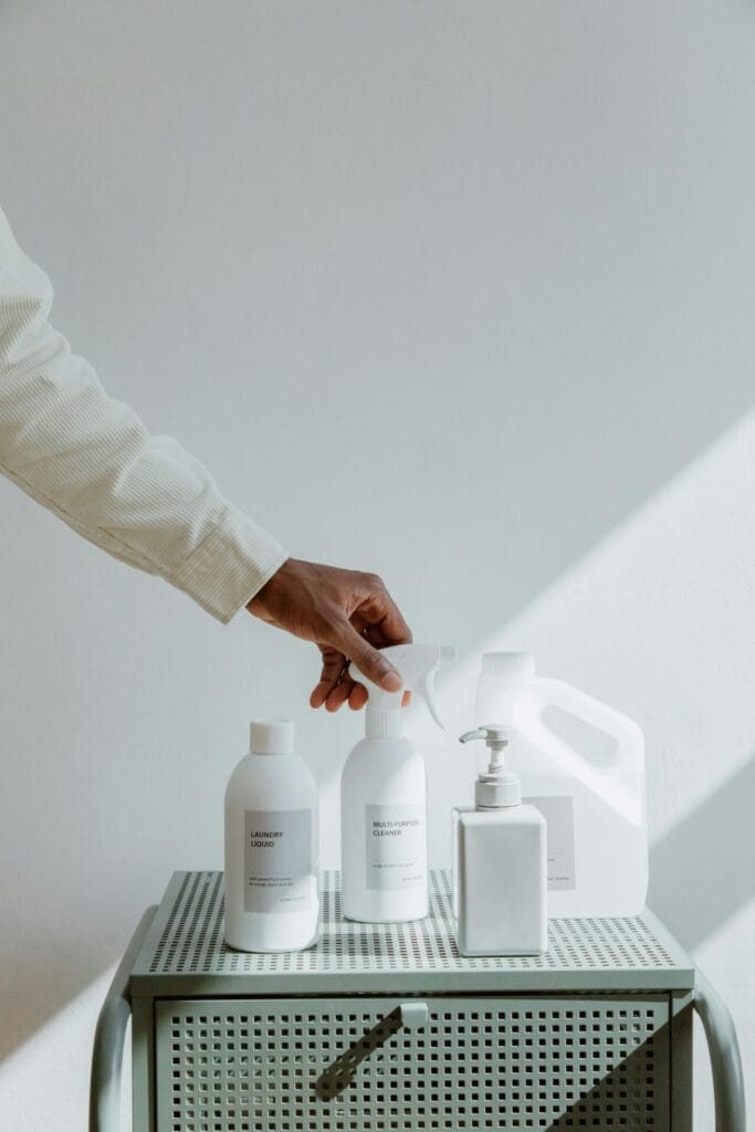 A hand reaches for minimalistic cleaning products in bright, airy lighting.