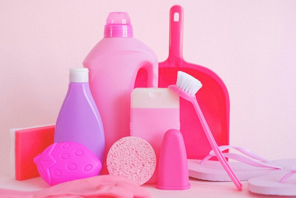 Assorted plastic containers with sponge and dustpan with brush for cleaning routine on pink background