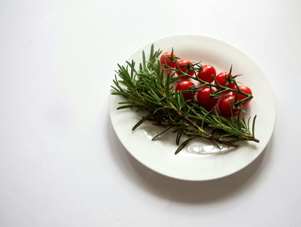 A minimalist setup of fresh rosemary and cherry tomatoes on a white plate.