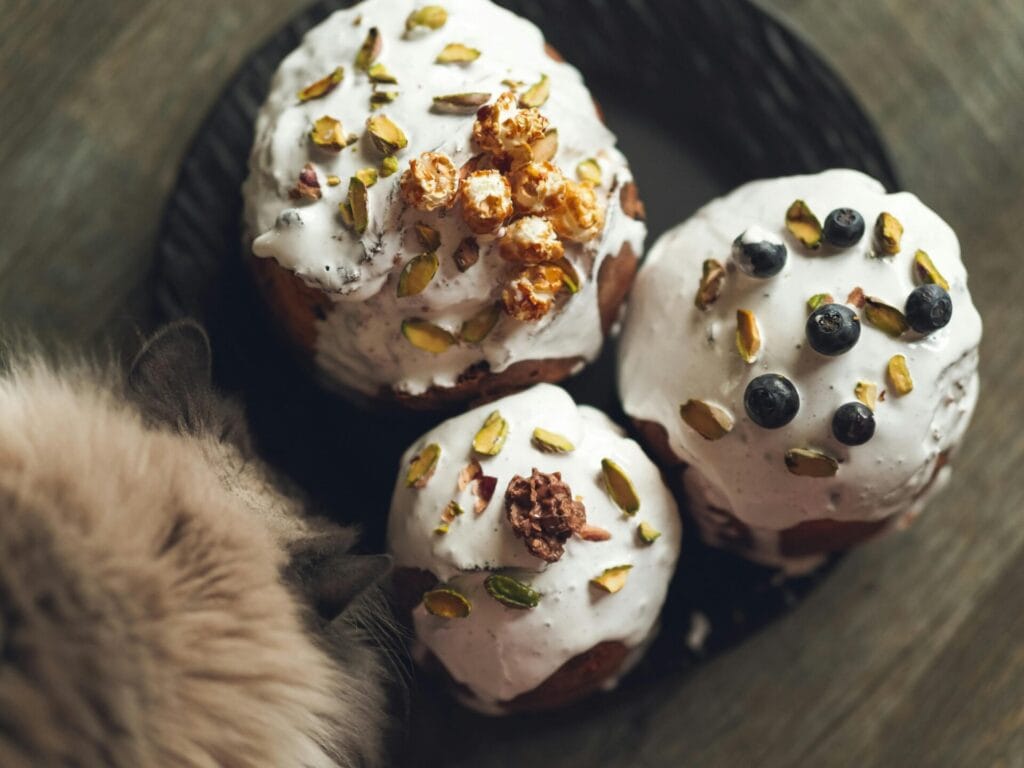 Close-up of festive baked goods topped with nuts and berries, accompanied by a fluffy cat.
